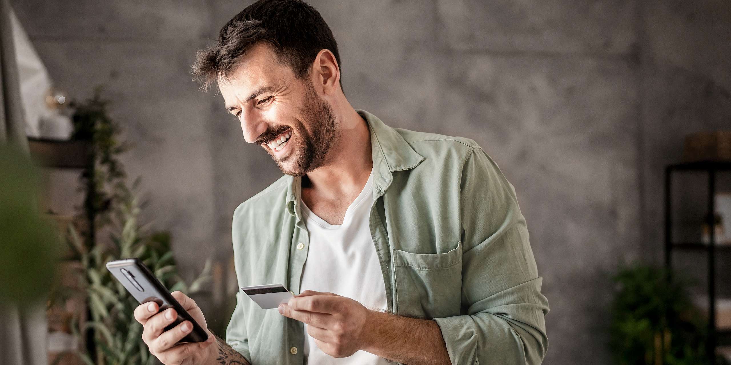Ein Mann hält ein Smartphone und eine Business Kreditkarte in der Hand.