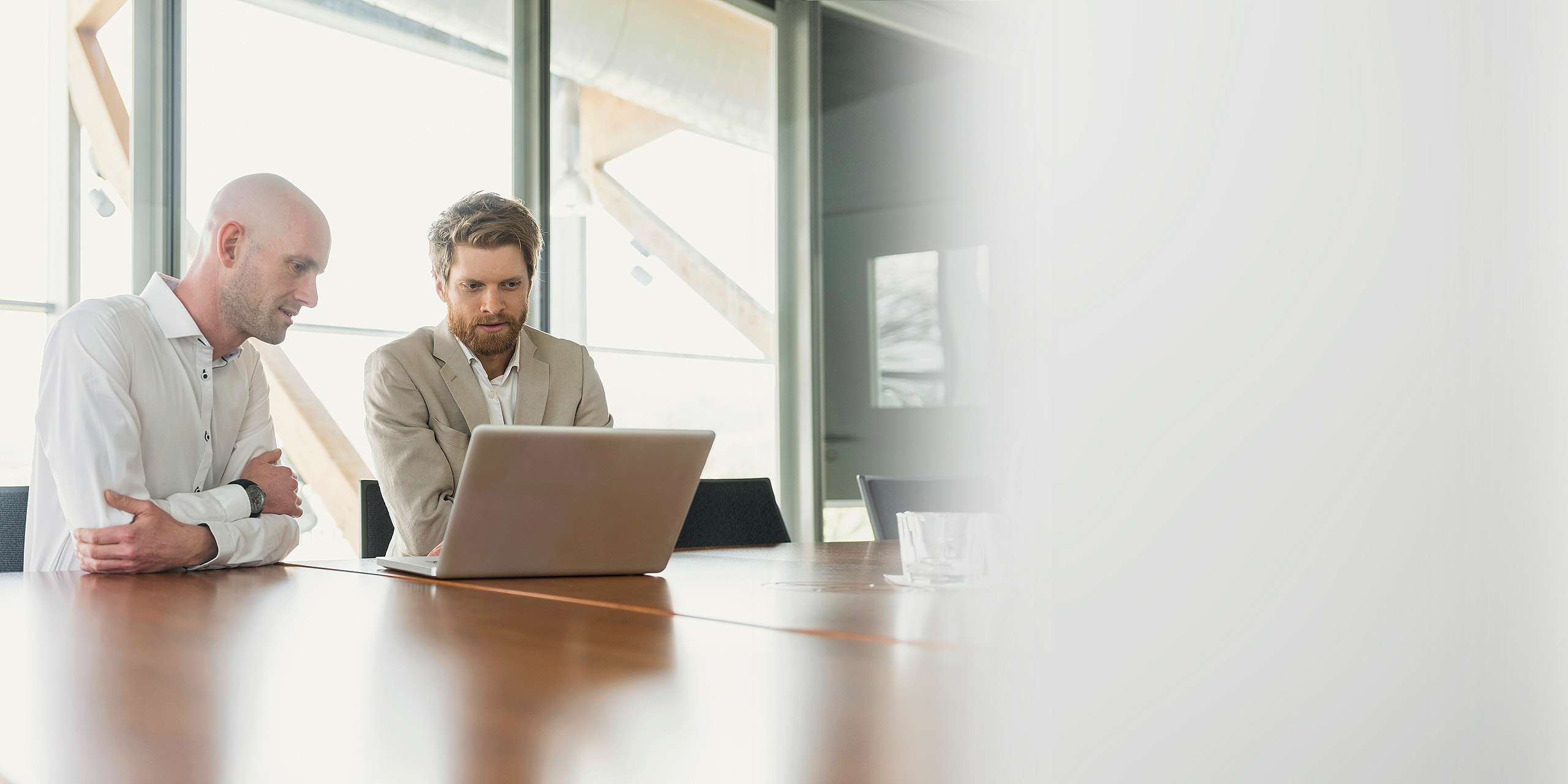 Zwei Männer in Business-Kleidung sitzen an einem Laptop in einem Konferenzraum